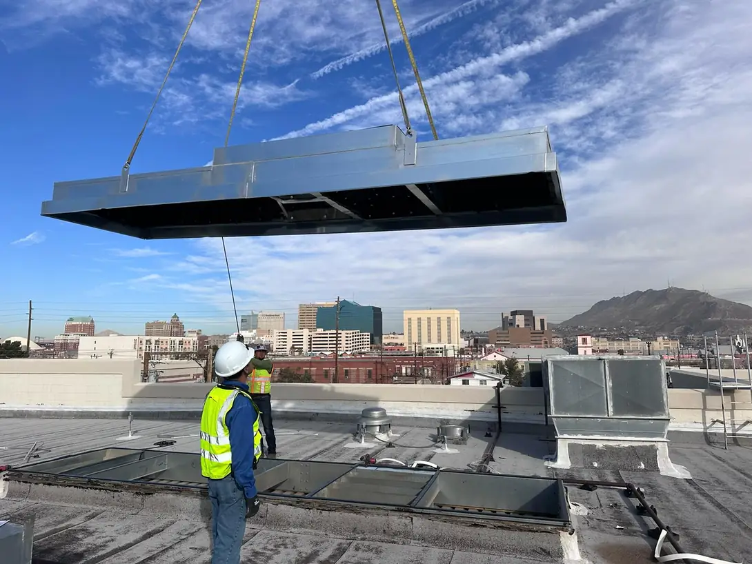 Commercial rooftop HVAC equipment being lifted above a roof